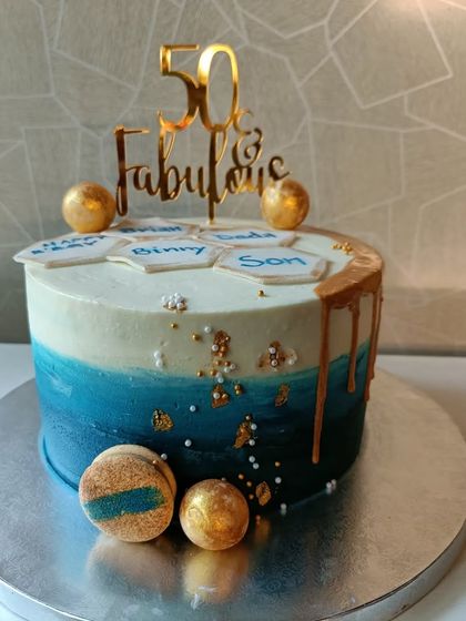A sophisticated cake for a "50 & Fabulous" celebration. The blue ombre effect, gold drip, and macarons create a modern and elegant look.