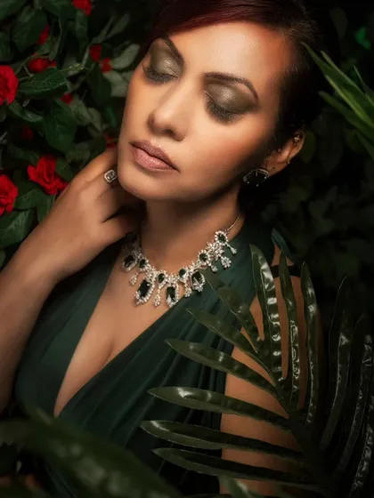 A close-up portrait set in a lush, green environment created with a combination of real and projected foliage. The soft lighting beautifully highlights the model's features and the delicate jewelry.