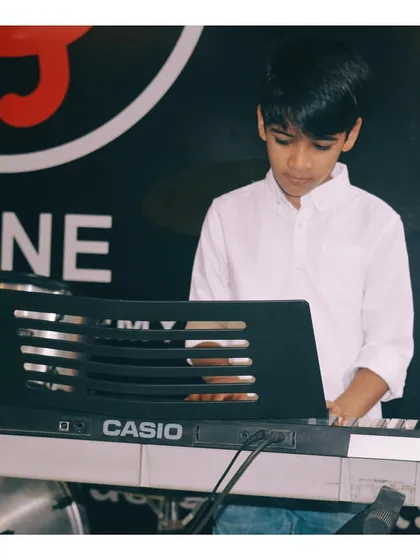 A young keyboard student practicing during a class. You can see his focus as he works on a piece, with the drums visible in the background, showing our multi-instrument environment.