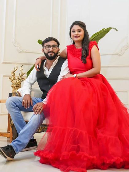 A relaxed and happy pre-wedding portrait. The bride-to-be is all smiles in a vibrant red ruffled gown, seated comfortably with her partner.