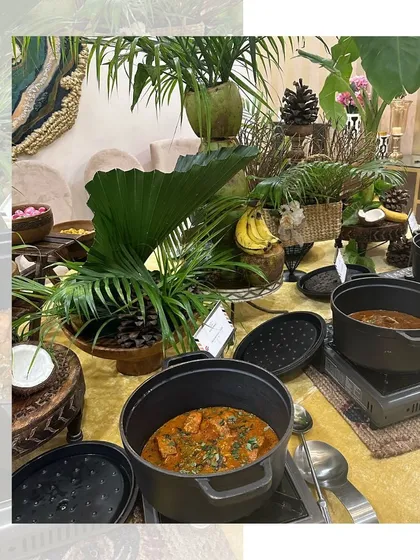 A tropical-themed hot buffet station, with lush green decor and food served in modern cast iron pots.