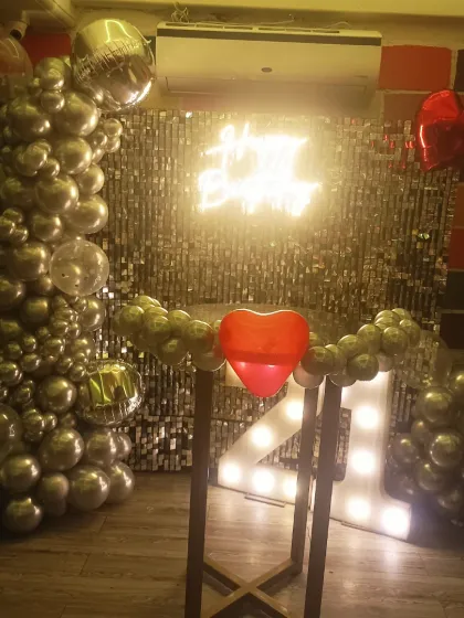 A close-up of a 21st birthday photo corner, featuring a silver shimmer wall, neon sign, and marquee numbers.