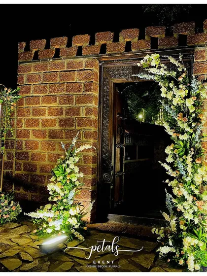 An entrance should be a prelude to the magic inside. This modern, broken arch design, illuminated against a rustic brick wall, creates a sophisticated and intriguing welcome for guests at an evening reception.