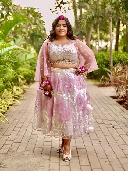 A full-length shot in a beautiful garden setting. The bride's makeup is fresh and bright, perfect for a daytime Haldi celebration.