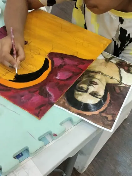 The painting is starting to take shape! This student is carefully blocking in the main colors and shapes of her portrait, following the reference image to guide her composition.
