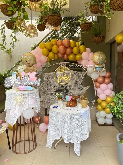 A wider angle of the rustic 'Oh Baby' baby shower, showing the complete setup with two decorated tables and a beautiful balloon arch in a well-lit space.