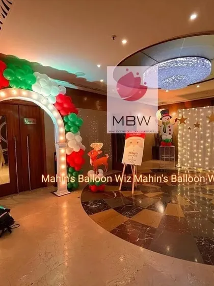 The entrance to the Christmas party, featuring a light-up arch with red and green balloons and a welcome sign with a snowman prop.