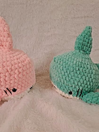 A pair of plush sharks in pink and mint green.