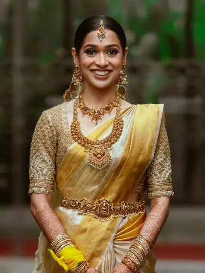 A smiling bride in her golden-yellow Kanchipuram saree and heavily embroidered blouse. This classic South Indian bridal look is both timeless and celebratory.