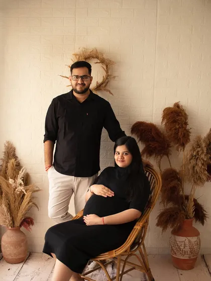A classic maternity portrait with a boho touch. The couple's dark outfits contrast beautifully with the earthy tones of the pampas grass and rattan chair.