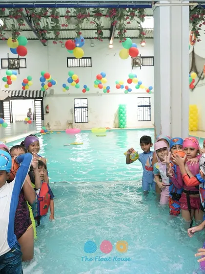 A train of happy kids playing games in the pool during a birthday party, with colorful balloons decorating the ceiling.