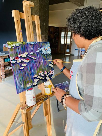 An adult student works at her easel, building up layers of color to create the illusion of light on water in her Monet-inspired piece.