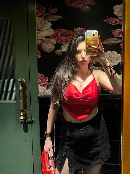 A bathroom mirror selfie in a red satin top and black mini skirt, a classic and confident party look.