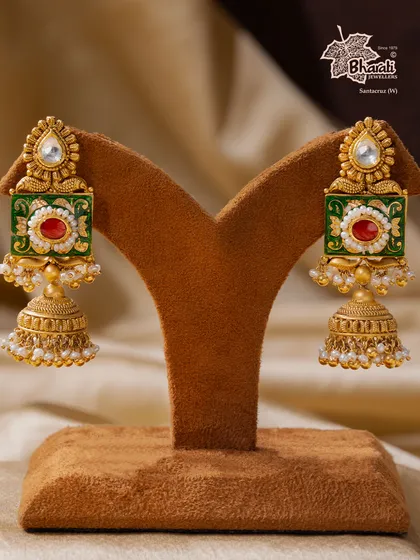 A tribute to India’s timeless artistry. These Meenakari jhumka earrings are hand-enameled with vibrant green and red floral motifs, framed in antique gold. The design is completed with a classic bell shape and delicate pearls, making them a regal addition to any ensemble.