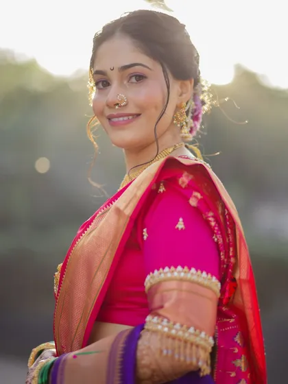 A sun-kissed portrait highlighting the bride's flawless makeup and joyful expression. The natural light beautifully captures the rich colors of her pink Nauvari saree.
