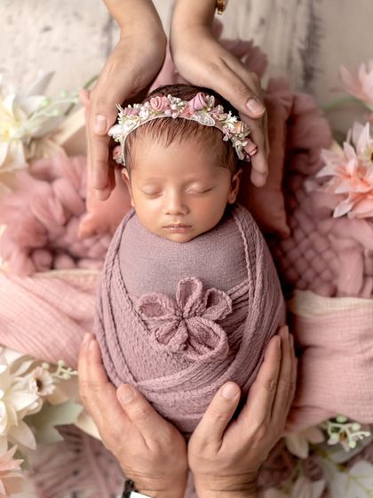 Held safely in loving hands. This shot, with a beautiful floral wrap and headband, emphasizes the delicacy and preciousness of a newborn.