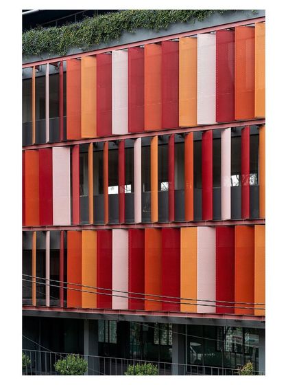 A detailed shot of the kinetic facade, showing the vertical metal panels in shades of red and orange. This system allows for dynamic control of heat and light.