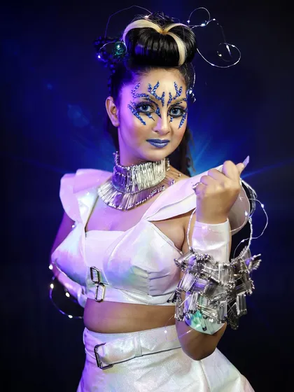 An ethereal, alien-like character with blue crystal makeup and a futuristic white outfit. I teach you how to use embellishments and lighting to create magical effects.