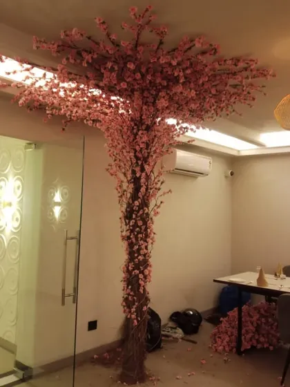 An artificial pink blossom tree being prepared for an installation, showing the intricate trunk and dense foliage.