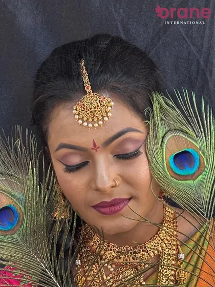 An artistic shot using peacock feathers to frame the face, enhancing the traditional aesthetic of the makeup.