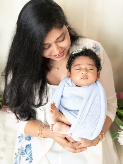 A mother gazes down with pure love at her sleeping newborn, cradled gently in her hands.