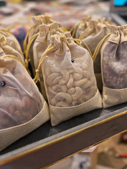 A closer look at the sheer jute potlis filled with high-quality nuts. The tiny evil eye bead on the drawstring is a subtle but meaningful touch that reinforces the theme throughout the entire collection.