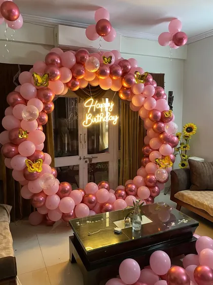 A living room decoration with a circular balloon arch in shades of pink and rose gold, adorned with butterfly stickers.