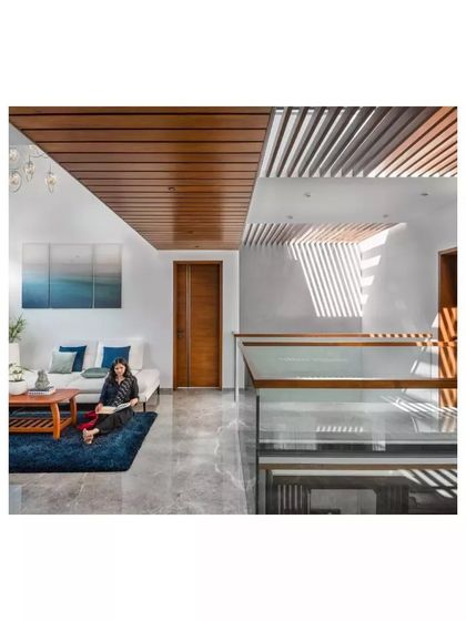 The upper living area in the Janani House uses a slatted wood ceiling and strategic openings to create patterns of light and shadow. The design provides a cozy, private space for the family to gather.