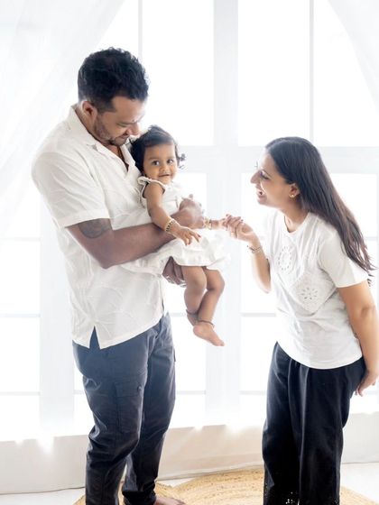 A candid family moment, with the mother playfully interacting with her daughter held by the father.