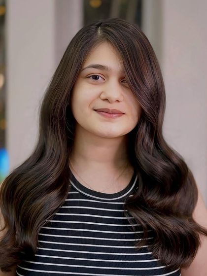 A youthful and fresh look with long, healthy brown hair styled in soft waves. The subtle highlights add a touch of sun-kissed dimension.