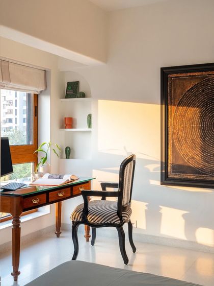 A dedicated study nook is carved out by the window, providing a quiet space for work. The vintage-style desk and striped chair are complemented by built-in shelves for display, all illuminated by natural light.