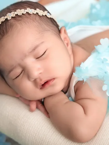 A close-up shot of a newborn baby girl sleeping peacefully, her head resting on her hands. The soft lighting and simple styling emphasize her delicate features and the tranquility of the moment.