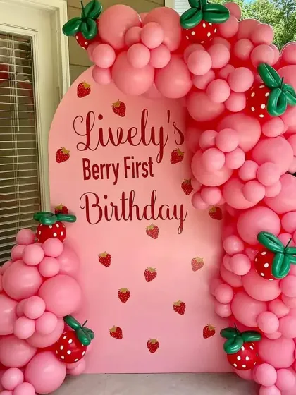 A unique "Berry First Birthday" with a strawberry theme, featuring a custom pink backdrop and a balloon garland with strawberry details.