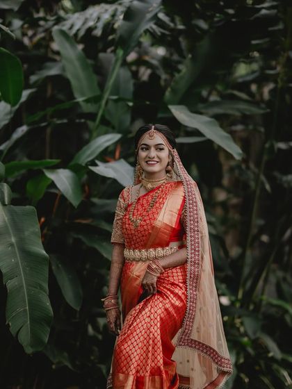 Tanu surrounded by lush greenery, her red saree creating a stunning contrast.