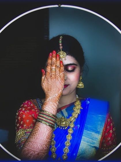 A creative shot highlighting the intricate henna and the bold eye makeup. The ring light frames her face, showing the details of her maang tikka and smokey eyeshadow.