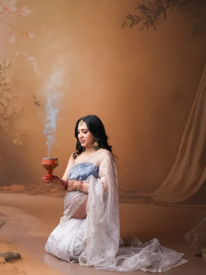 A spiritual and serene portrait. This unique concept features the mother-to-be in a modern take on a saree, holding a traditional incense burner. The soft lighting and artistic elements create a peaceful and meaningful image.