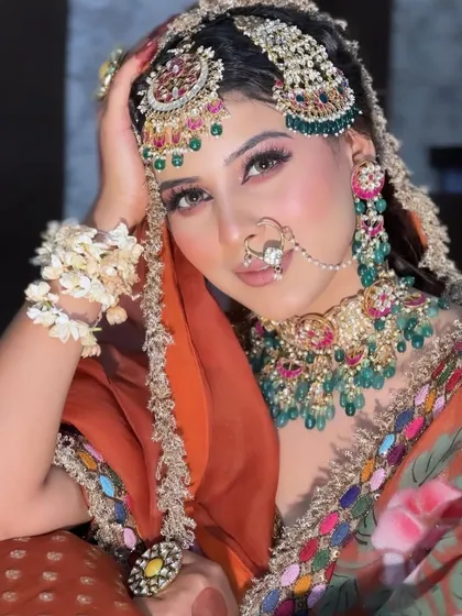 A regal and powerful bridal portrait. This look features heavy, traditional jewelry with green accents, paired with perfectly sculpted makeup and a confident gaze.