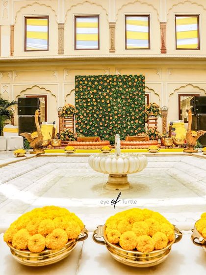 The grand Haldi decor setup in a palace courtyard. The vibrant yellow marigolds and traditional elements create a festive and royal atmosphere.