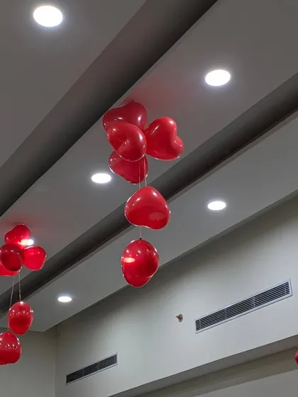 Red heart-shaped balloon bouquets hanging from the ceiling. This is a simple and cost-effective way to decorate a large office or clinic space for Valentine's Day or health-themed events.