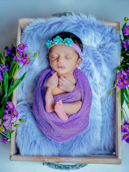 This image from the purple-themed series features a different pose, with the baby's hands gently framing her face. The turquoise floral headband adds a lovely contrasting detail to the portrait.
