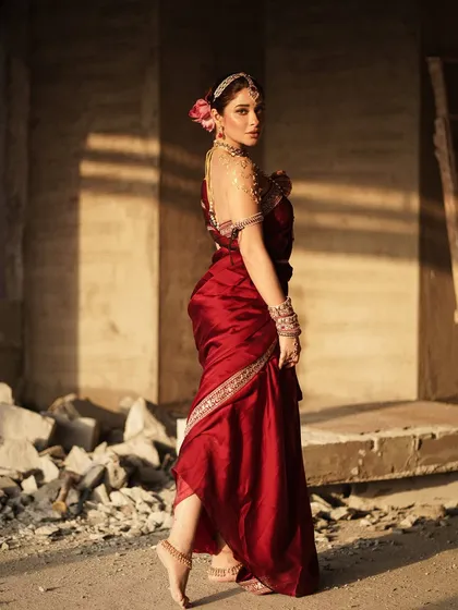 A full-length profile shot that emphasizes the elegant posture and the flow of the red saree. The single rose in her hair adds a classic romantic element to this traditional look.