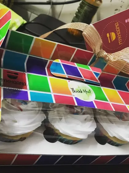 Gifting made easy and colorful. Here are three of our home-baked cupcakes with white frosting, presented in a vibrant, multi-colored box that’s perfect for surprising a loved one.