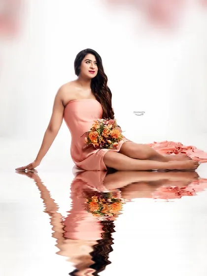 A dreamy portrait with soft pink floral elements framing the image. The client's relaxed pose in the peach gown and the water reflection create a truly romantic and ethereal feel.
