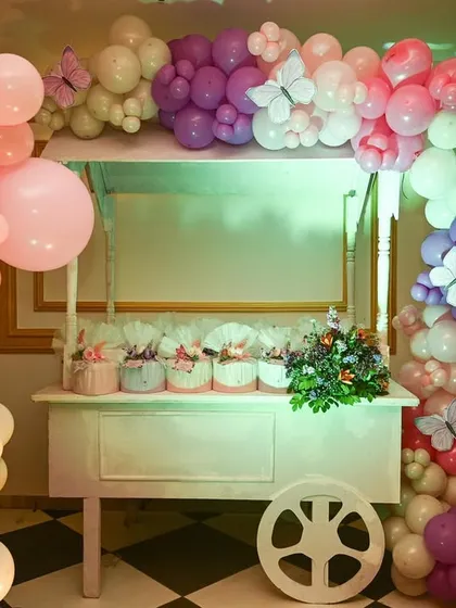 A charming white cart serves as a favor station, decorated with a cascading balloon arch dotted with small butterflies.