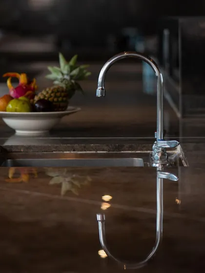 An on-location shot of a T&S Brass faucet in a high-end kitchen setting. The reflection on the glossy countertop and the bowl of fruit in the background create a sophisticated, real-world context for the product.