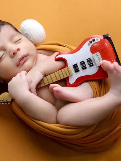 A close-up of our little musician, wrapped in a warm mustard-colored swaddle. The simple background keeps all the attention on the sleeping baby.