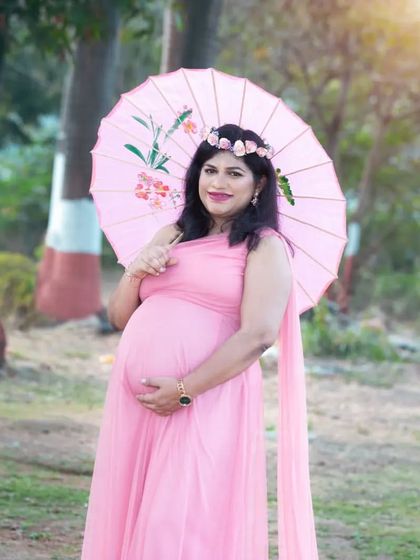 A whimsical portrait with a pink paper umbrella. This prop, along with the floral crown and pink gown, adds a touch of playful charm to the maternity shoot.