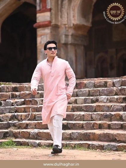 A model confidently walks down stone steps in a pink kurta and white trousers, showcasing the comfortable fit and modern styling.