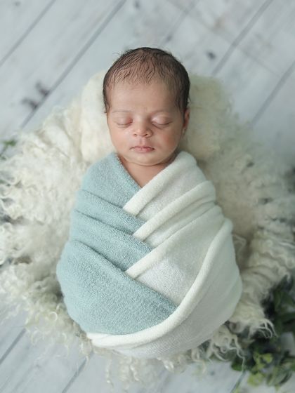 A beautifully swaddled newborn in a two-toned wrap, resting on a soft fur rug. This top-down angle is a classic way to show off the baby's peaceful state and perfect form.