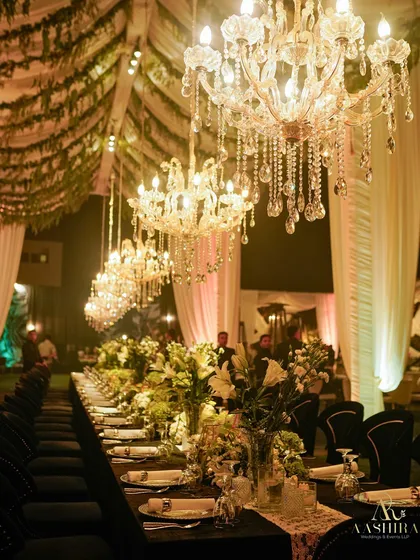 A long shot of the banquet dining setup, showing the dramatic effect of the row of crystal chandeliers hanging over the elegantly dressed table.